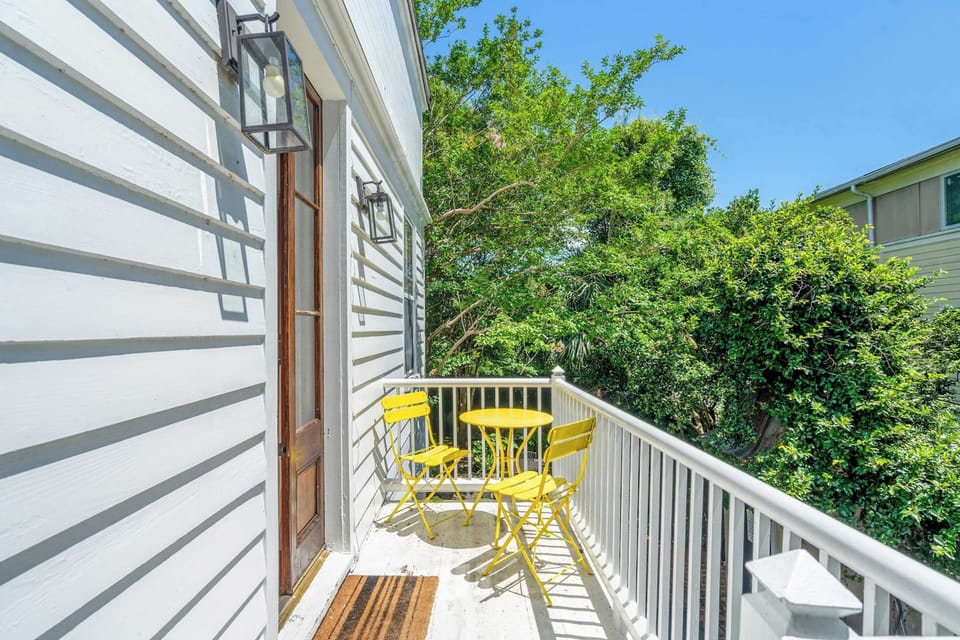 The charming exterior featuring a bright yellow bistro table, perfect for enjoying a morning coffee or an evening drink while overlooking the serene pool and lush courtyard below.