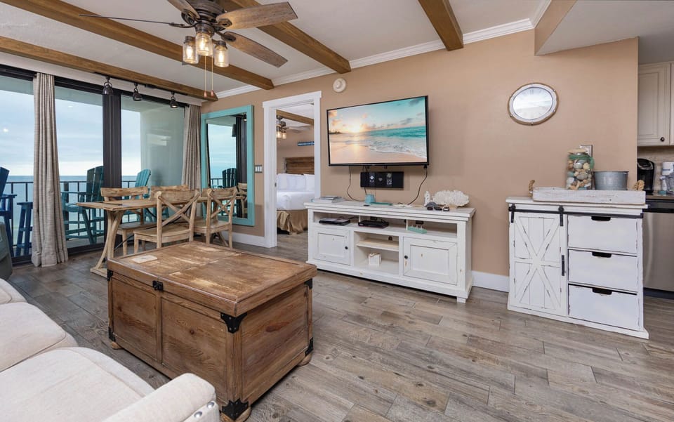 Bright living area featuring a cozy sofa with queen sleeper, rustic coffee table, and a view of the beachfront balcony