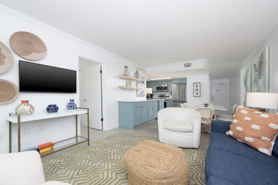 This living area features a sleek TV, colorful decor, and a cozy vibe with a view of the inviting kitchen space
