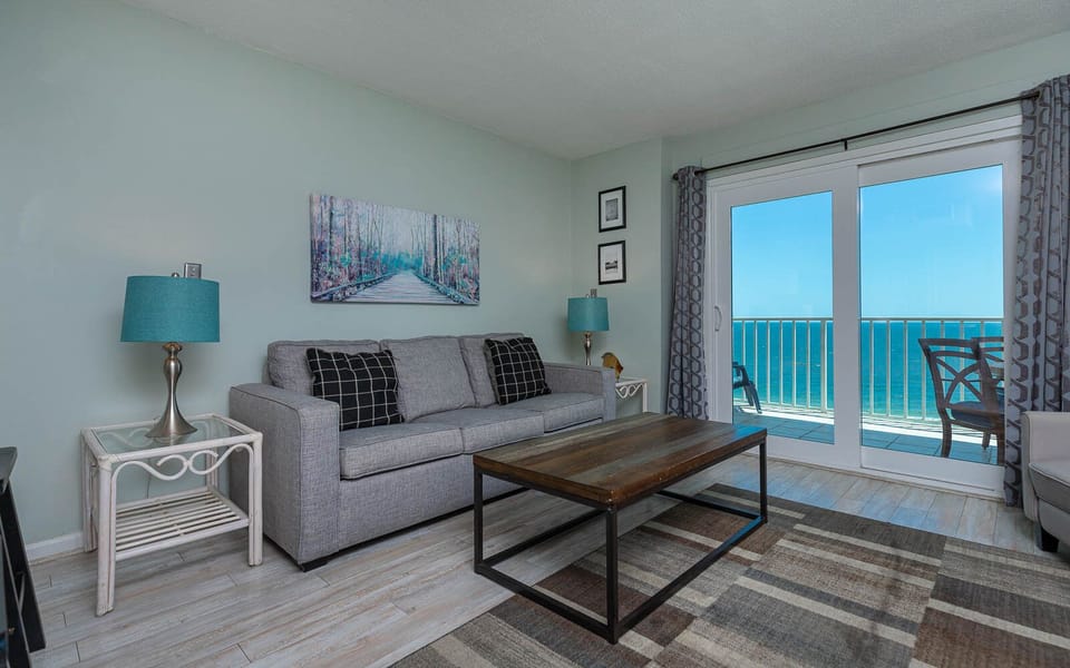 The living area features a cozy gray sofa, a stylish coffee table, and stunning beachfront views through large sliding doors