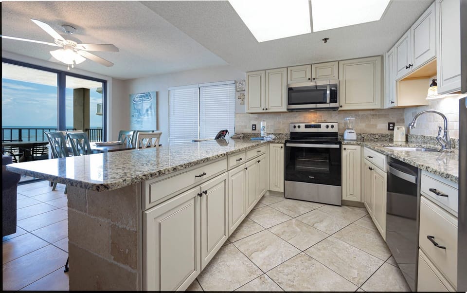 The kitchen features stainless appliances, granite countertops, coffee maker, and a beautiful beach view from the dining area