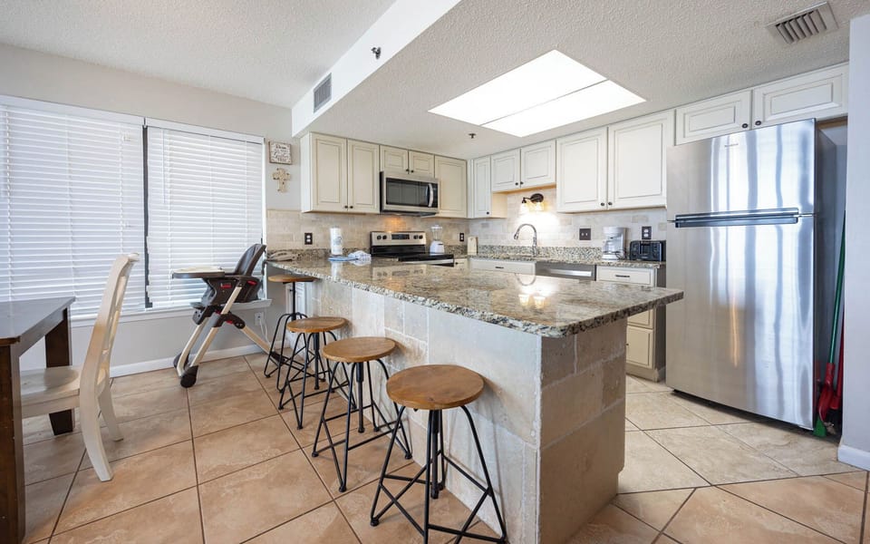 The kitchen features stainless appliances, granite countertops, and a breakfast bar with stools and an infant feeding chair