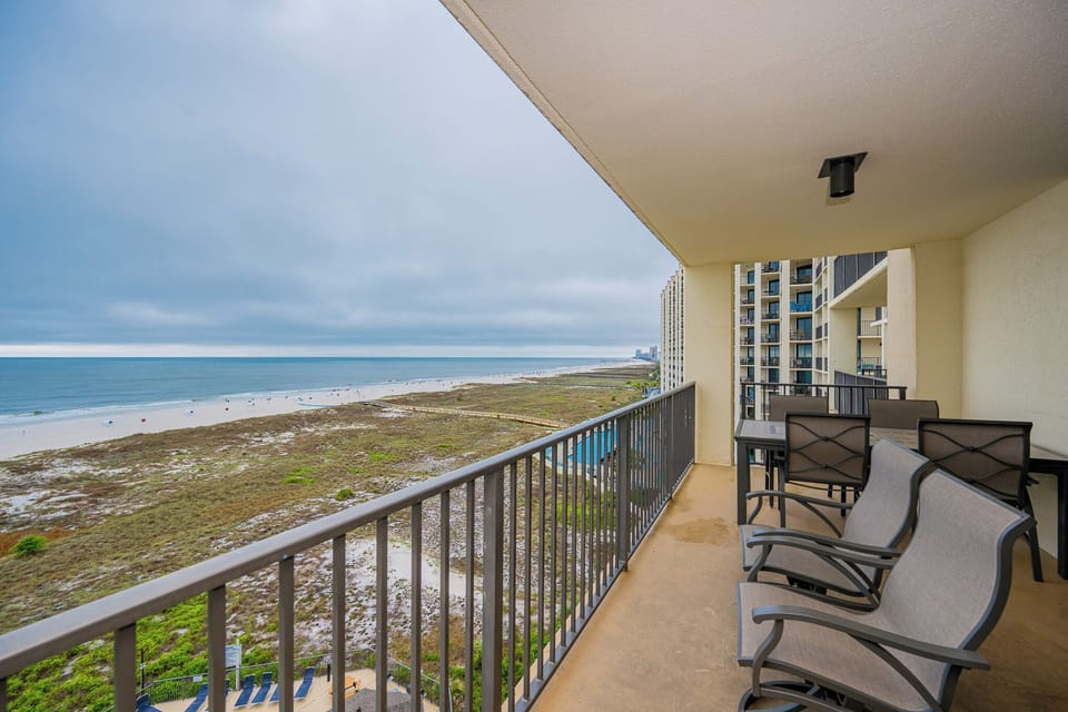 Spacious balcony with seating offers a serene view of the beach and gentle waves, perfect for relaxing moments outdoors
