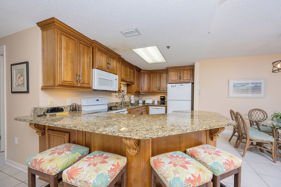 Warm wooden cabinetry complements the spacious breakfast bar with colorful stools, creating an inviting kitchen space