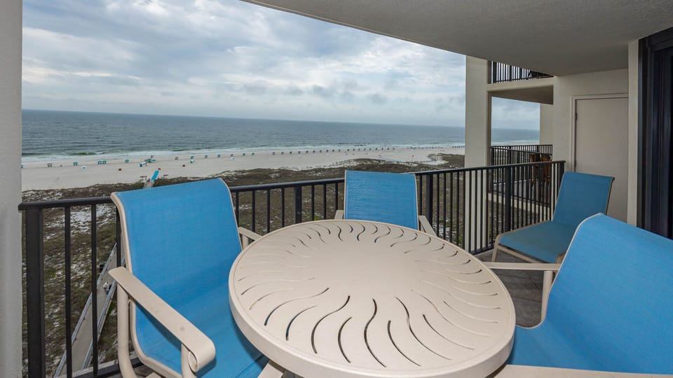Balcony seating offers a serene view of the beach with turquoise chairs and a round table, perfect for relaxation