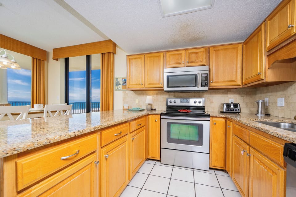 Bright wooden cabinetry complements the granite countertops in this kitchen, featuring a breakfast bar and views of the beach