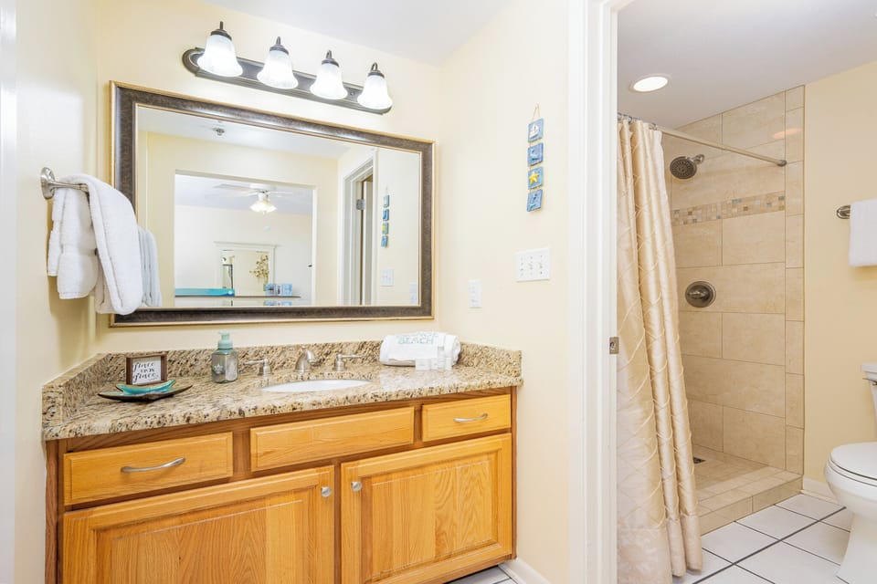 Warm wood cabinetry complements the granite countertop and illuminated mirror in this master bathroom with a walk-in shower