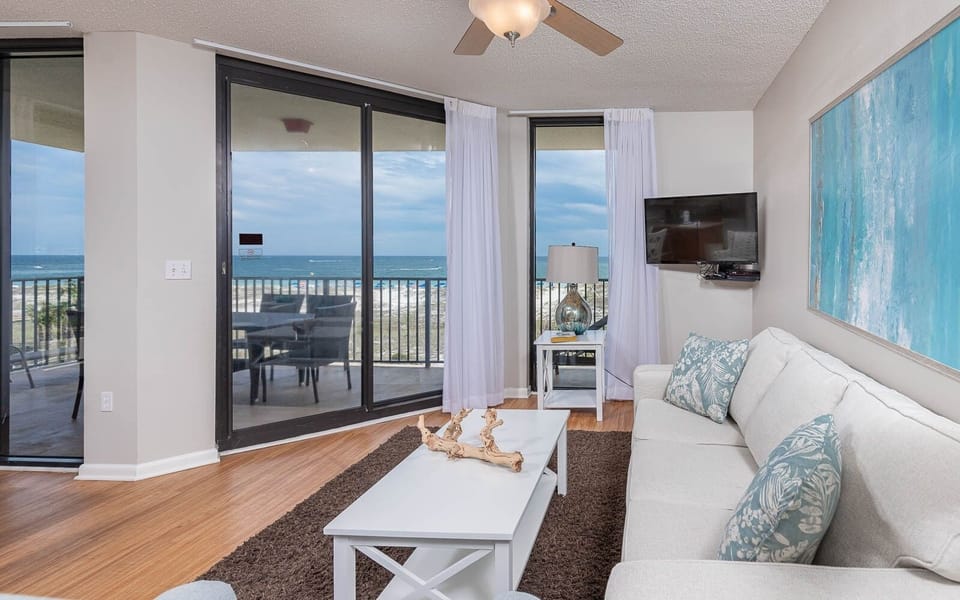 Cozy living area features a light sofa with queen sleeper, a TV, and stunning views of the beach from the balcony