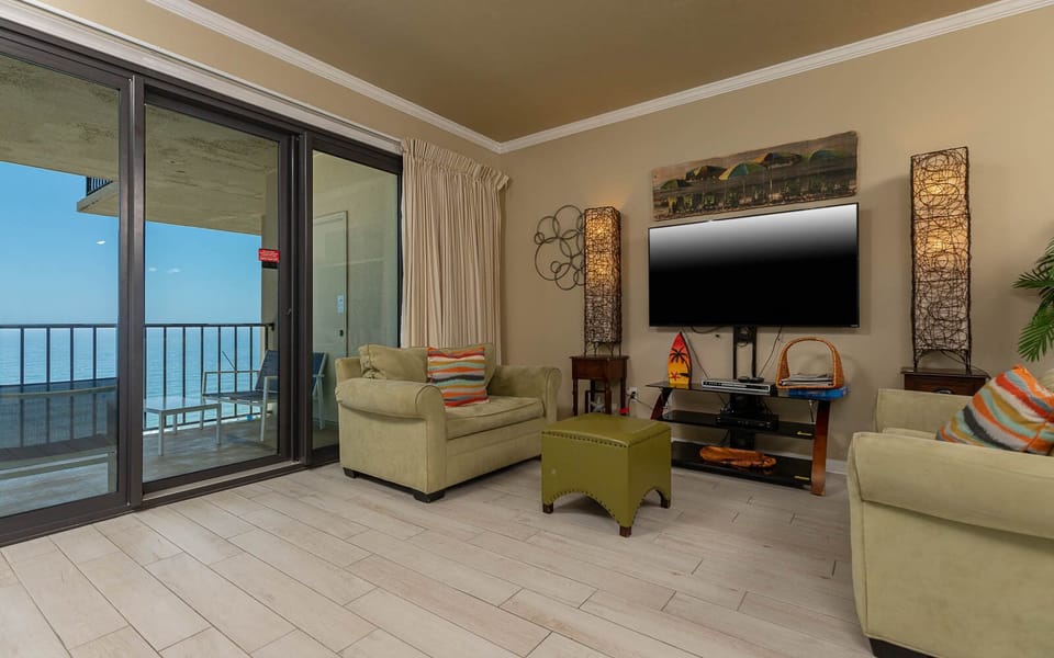 The living area features a large TV, colorful accents, queen sofa-sleeper, and a balcony with a beautiful beach view