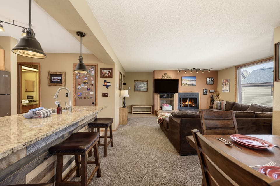 A cozy living space featuring a kitchen with a breakfast bar and stools, a fireplace, a TV, and a brown sectional sleeper sofa.