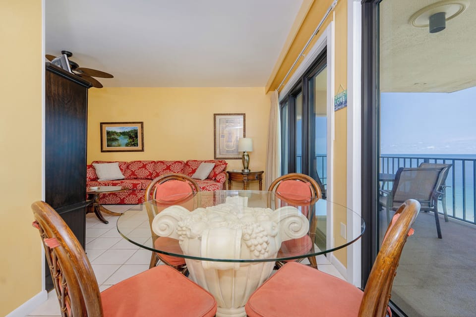The living area features a glass dining table, a vibrant red sofa, and a breathtaking view from the balcony