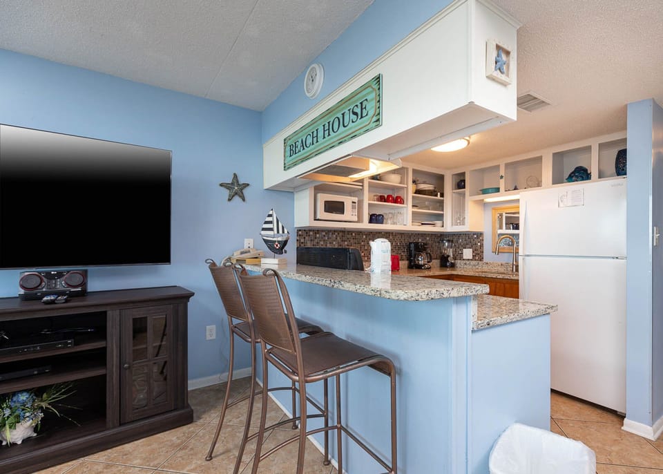 This inviting kitchen features granite countertops and a seating area below a beach house sign for enjoying meals together