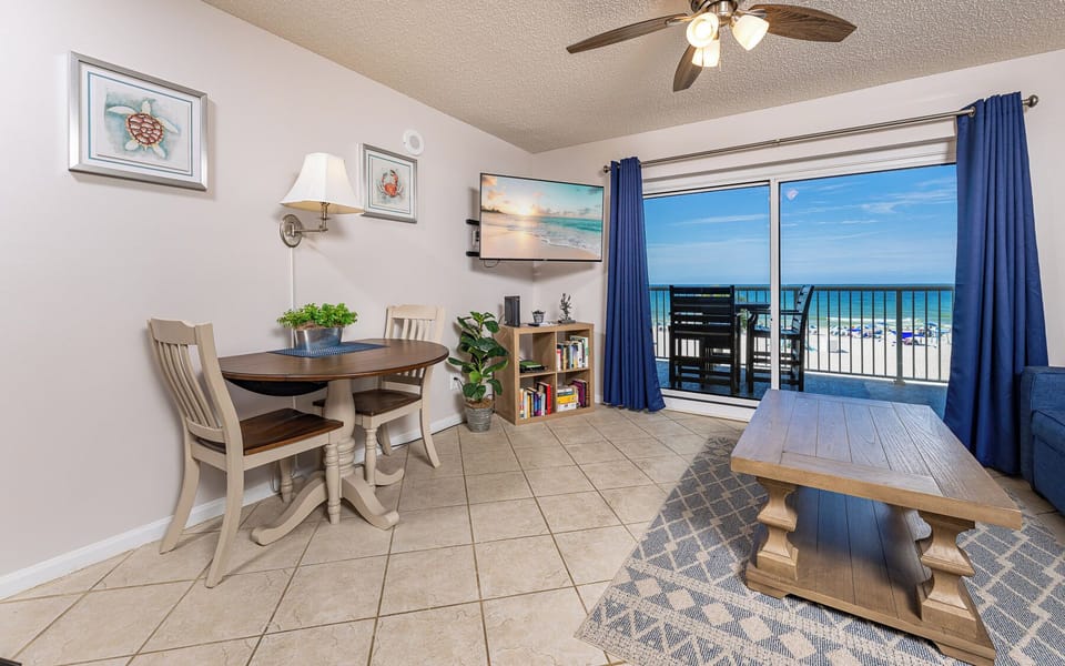 This cozy dining area features a TV, a table for meals, and a stunning view of the beachfront through sliding glass doors