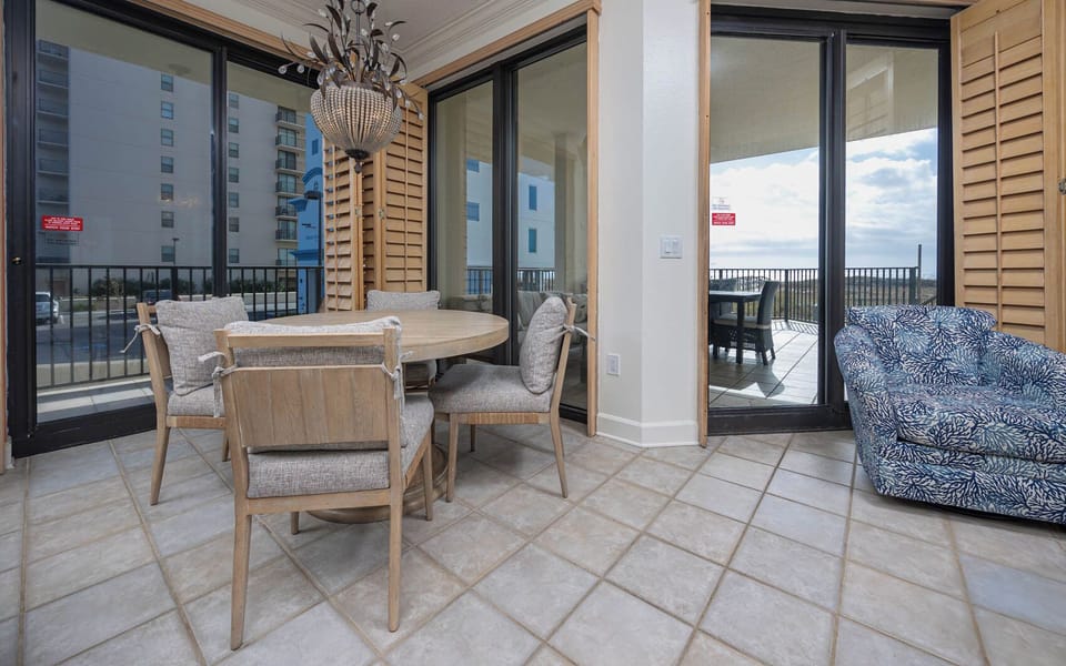 Dining area features a round table with stylish chairs and a cozy blue patterned chair, leading to a balcony view