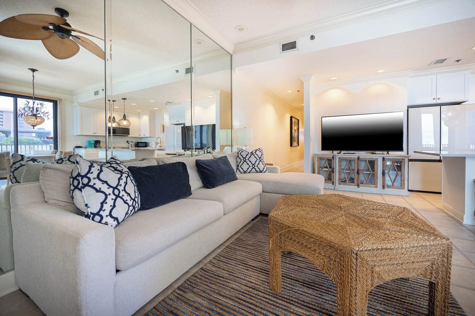 Cozy living area features a light-colored sofa with queen sleeper, a woven coffee table, and a view of the kitchen