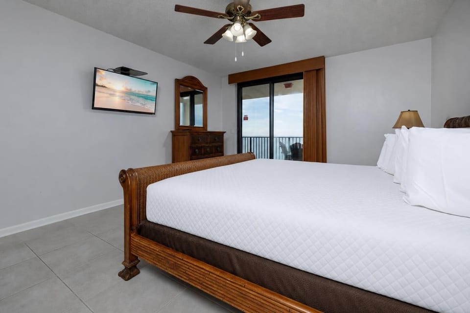 Rest in the serene master suite, featuring a cozy king bed, a TV for entertainment, and balcony doors to the beach view