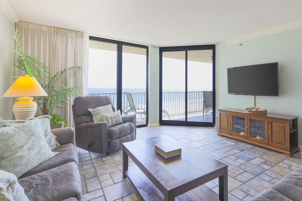 Cozy living area features a plush sofa, recliner, and a view of the beach through large sliding glass doors