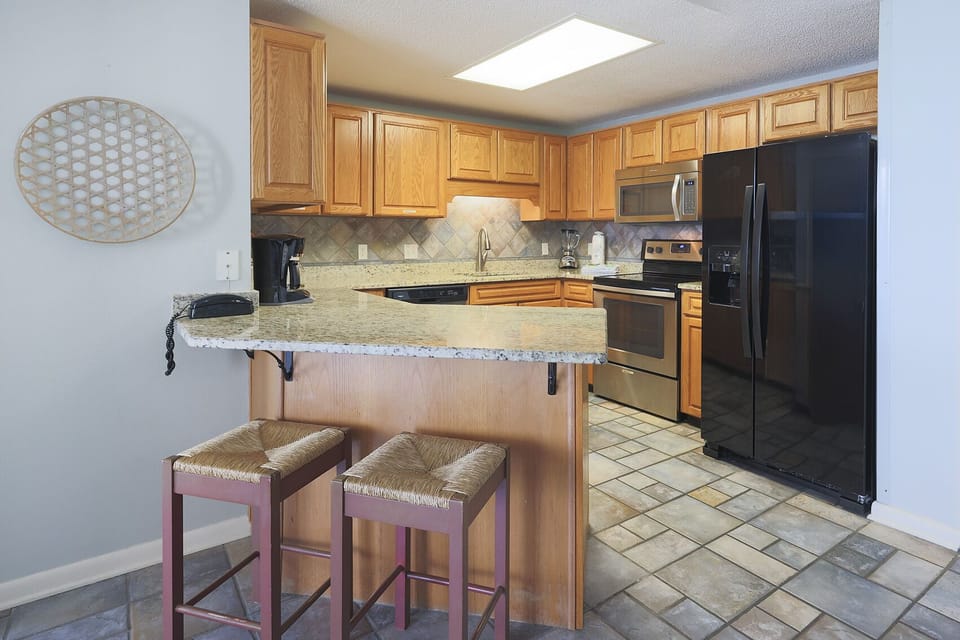 Warm wood cabinetry complements the granite countertops in this inviting kitchen, featuring a breakfast bar with two stools