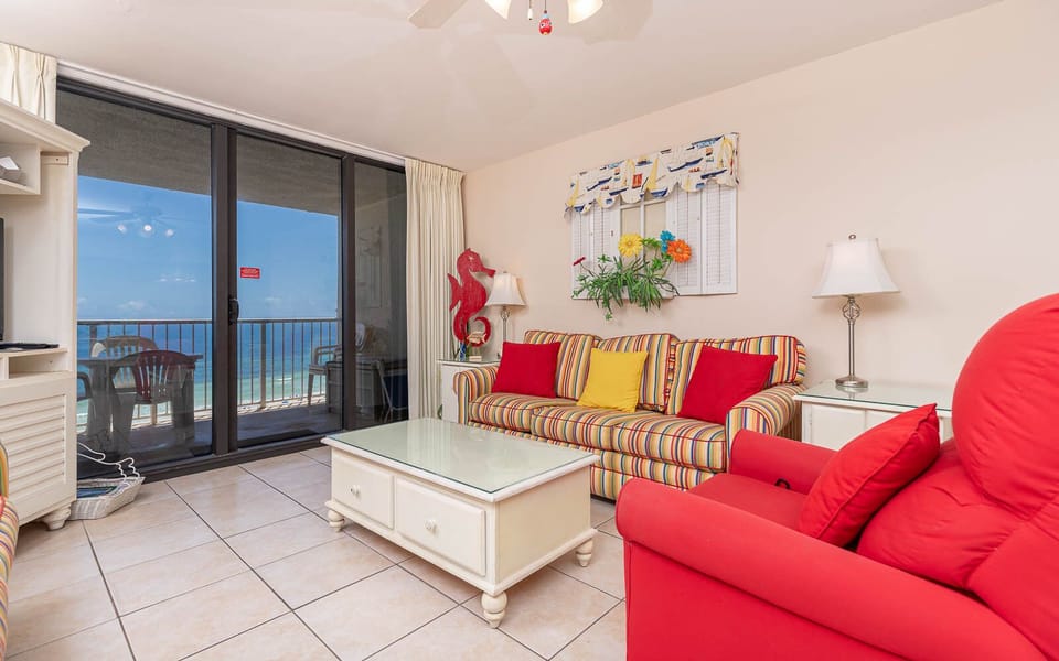 The living area features colorful striped seating, a glass-top coffee table, and a stunning beach view through sliding doors