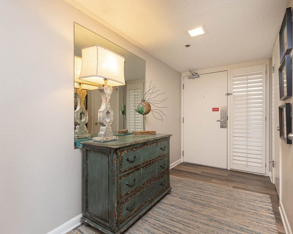 Step into a welcoming entryway featuring a stylish dresser, a decorative lamp, and natural light from the entry door