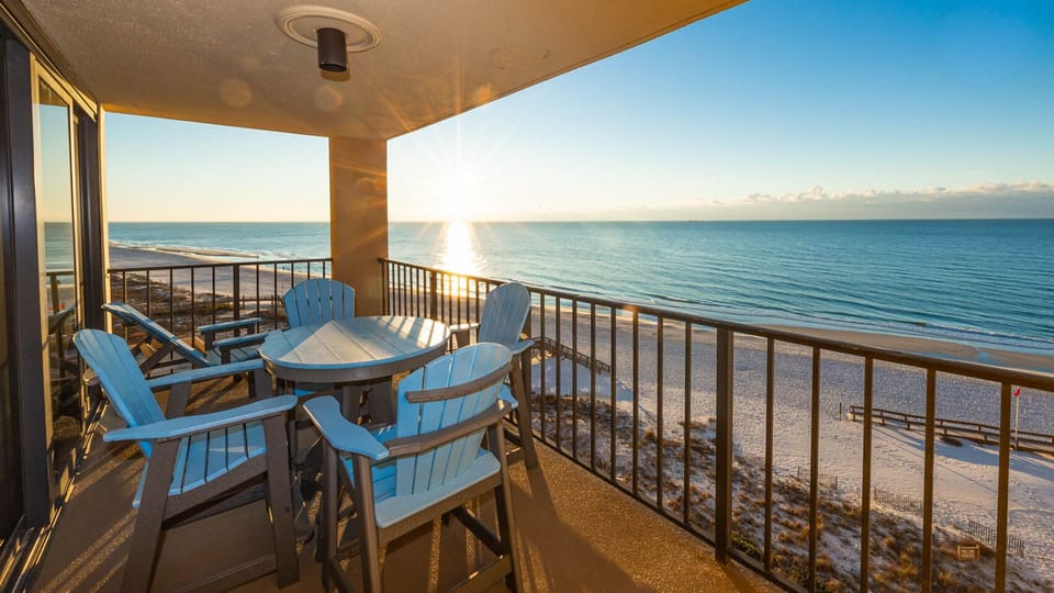 This balcony features a round table and blue Adirondack chairs, perfect for enjoying breathtaking views at sunset