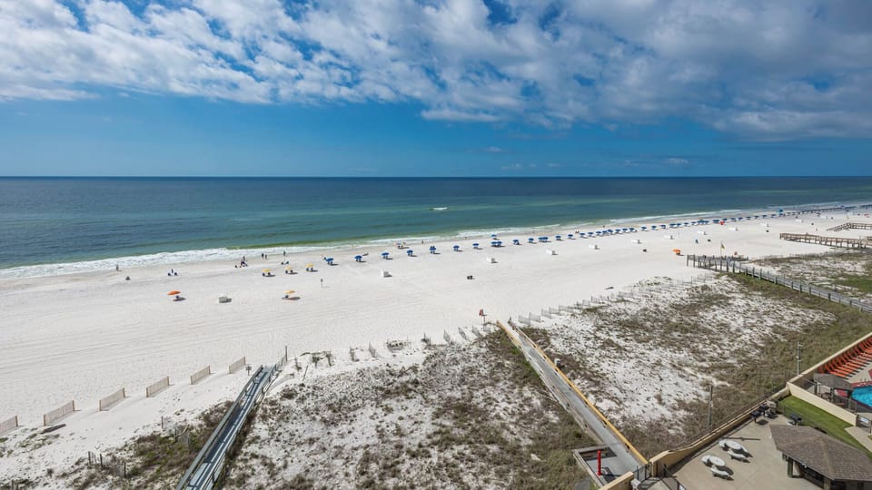 Expansive beachfront view showcases soft white sand and colorful umbrellas, inviting relaxation and enjoyment by the water