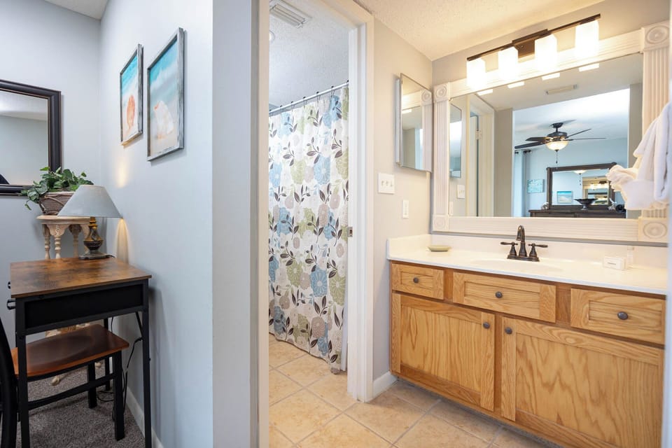 Master bath featuring a spacious vanity with wooden cabinetry, a decorative mirror, and a colorful floral shower curtain