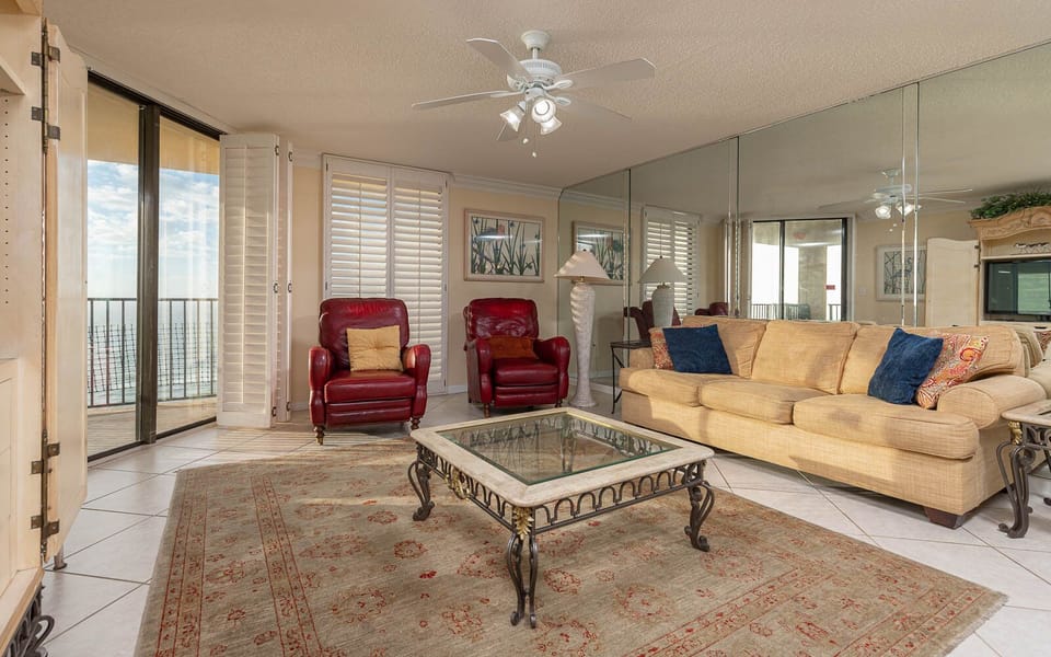 The living area features a cozy sofa with queen sleeper, two red armchairs, and a glass-top coffee table