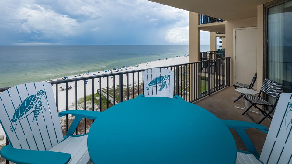 A turquoise table and chairs on the balcony offer a perfect spot to enjoy views of the beach and gentle waves below