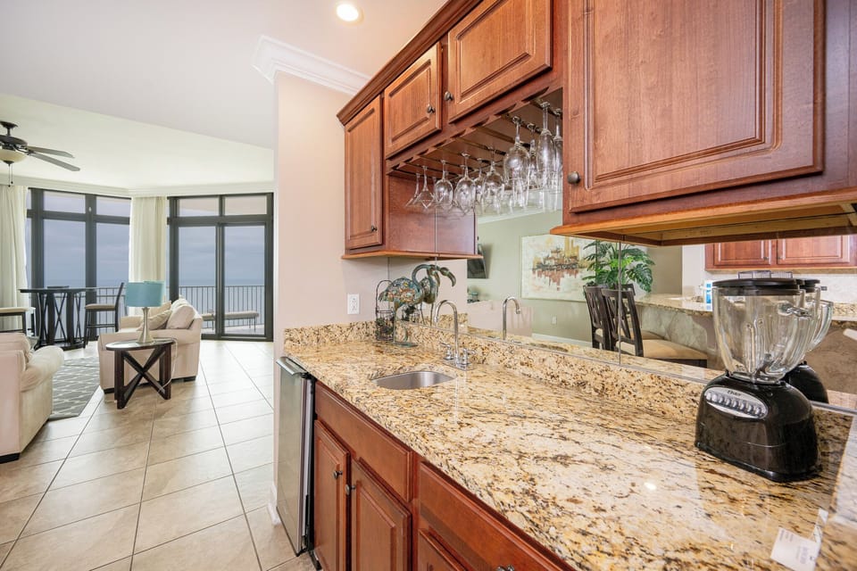 Wet bar area with granite countertops, stainless ice-maker, blender, and a view of the cozy living area beyond