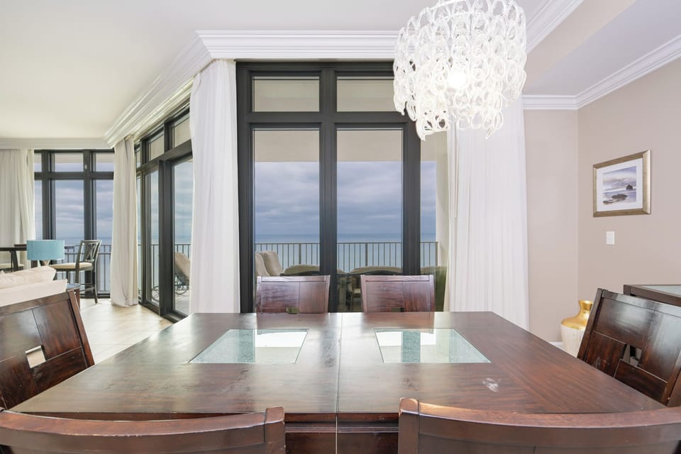 Enjoy breathtaking views from this elegant dining area featuring a stylish table and large windows draped in soft curtains