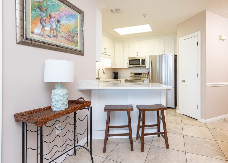 Enjoy casual dining at the breakfast bar with two wooden stools, complemented by a vibrant coastal artwork nearby