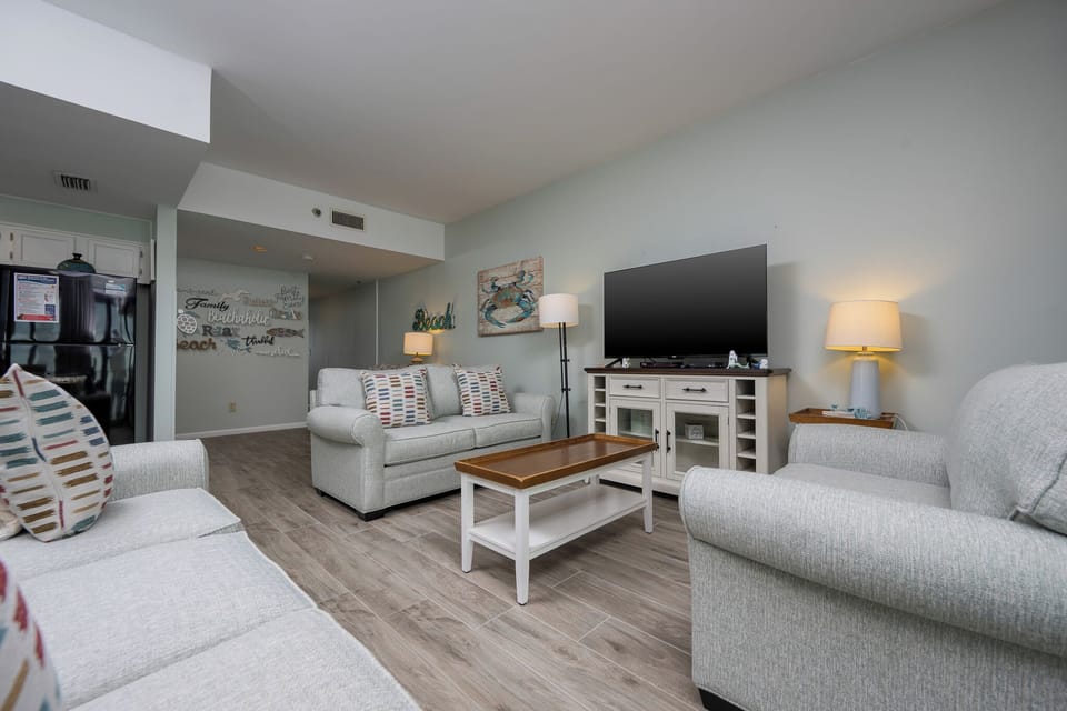 The living area features a comfortable sofa, a large TV, and beach-themed decor, perfect for relaxation