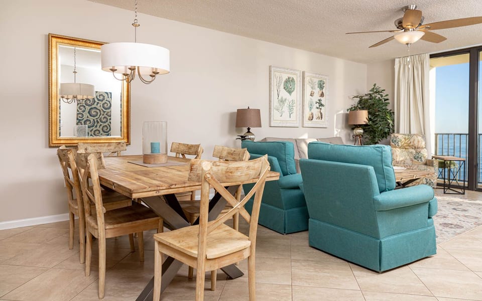 Cozy dining area features a rustic wooden table, stylish teal chairs, and a view of the beach through large sliding doors