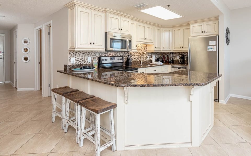 Bright and inviting kitchen features a spacious counter, wood bar stools, and modern appliances, perfect for vacation meals