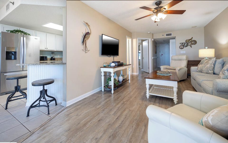 Cozy living area features a light-colored sofa and armchair, a wooden coffee table, and a breakfast bar with seating