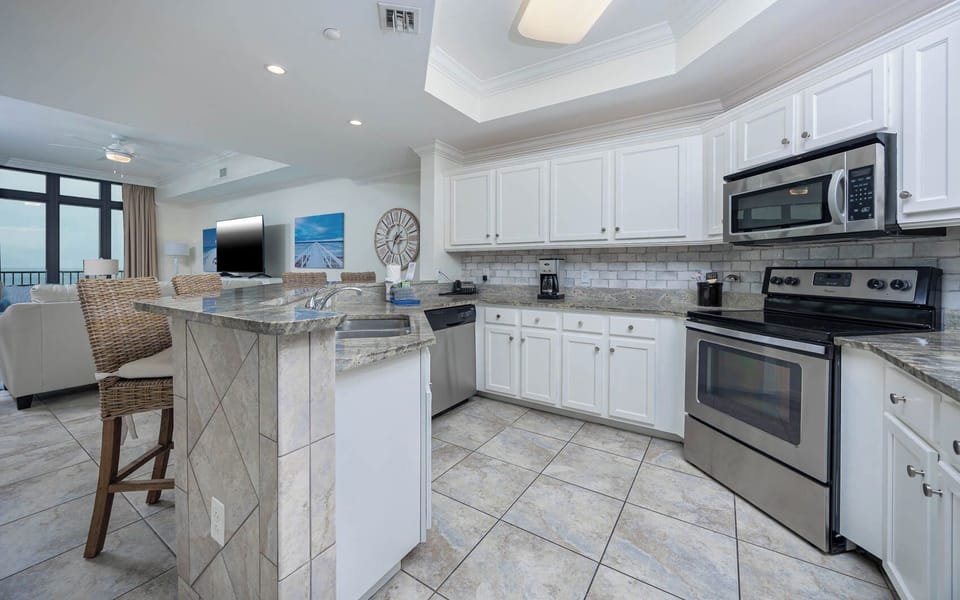 This stylish kitchen features stainless and granite with a sleek backsplash and a view of the beach with an elegant touch