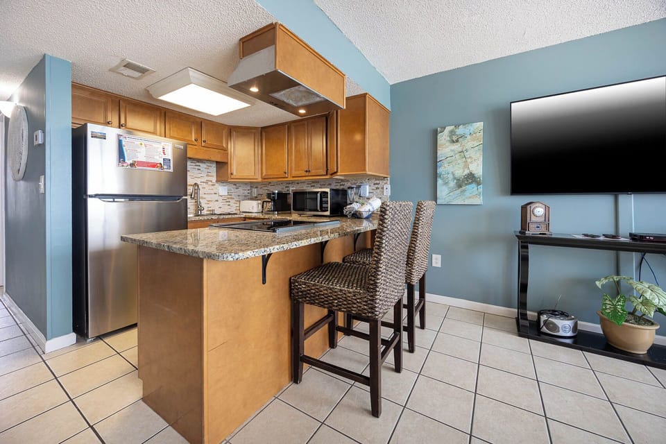 The kitchen features granite countertops, stainless appliances, and a cozy bar with two stools, perfect for casual dining