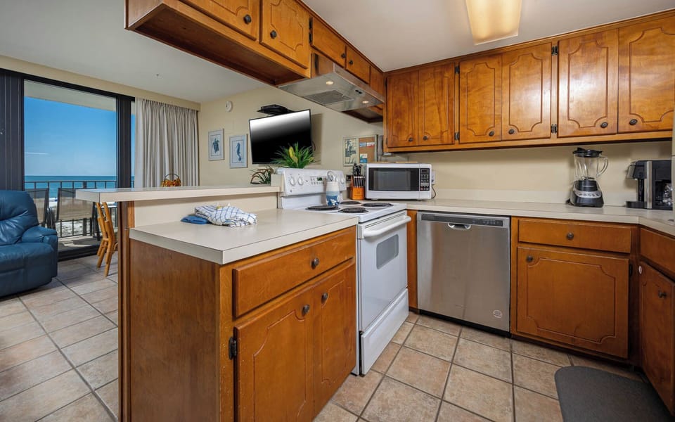 The kitchen features wooden cabinetry, convenient appliances, and a stunning beachfront view from the adjacent seating area