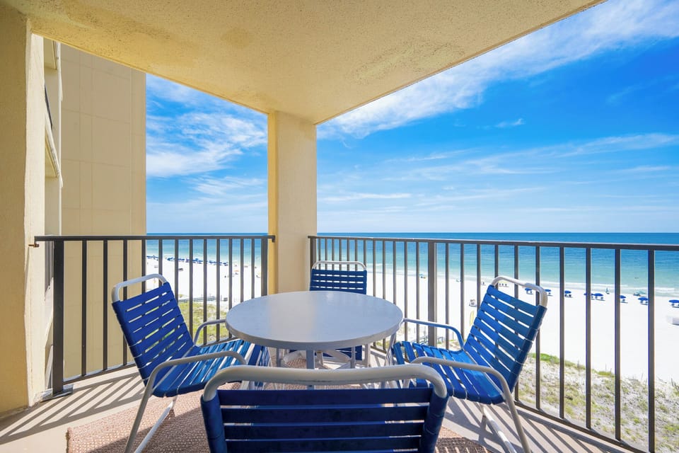 Enjoy a relaxing moment on the balcony with blue seating and a view of the white sand beach and tranquil waters