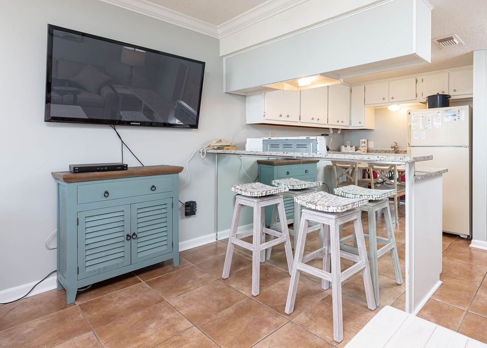 The space features a stylish seating area with a large TV and a well-equipped kitchen, perfect for relaxing and dining
