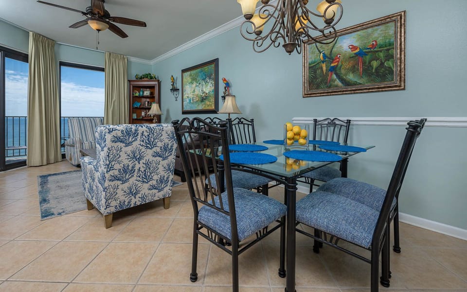 Bright dining area features a glass table with blue placemats, surrounded by stylish chairs, and offers views of the gulf