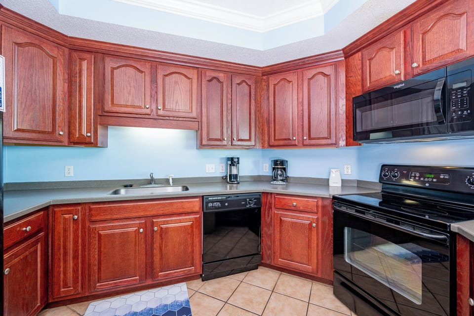 Inviting kitchen featuring rich wooden cabinets, black appliances, and a delightful hexagon-patterned rug