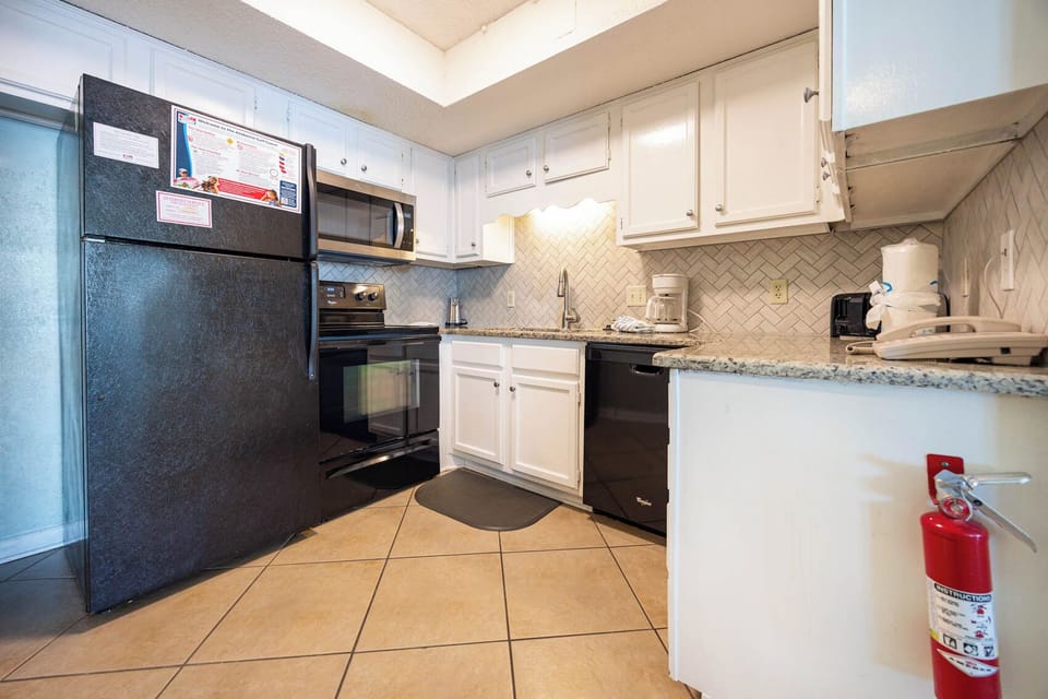 The kitchen features sleek black and stainless appliances, coffee maker, and granite countertops for a delightful experience
