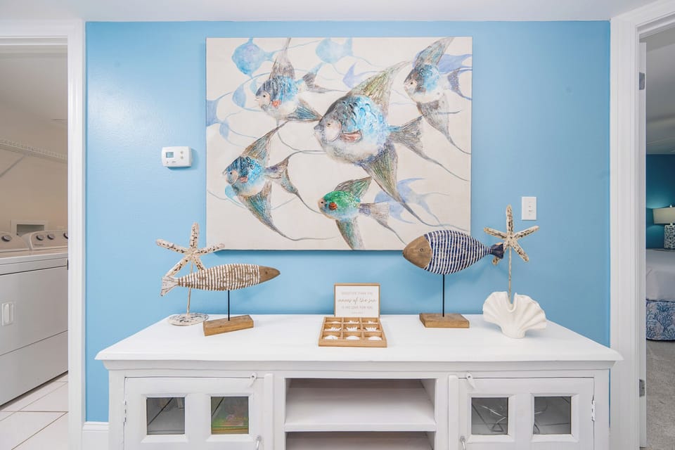 Colorful fish artwork complements a coastal console table adorned with decorative sea-inspired accents in a serene space