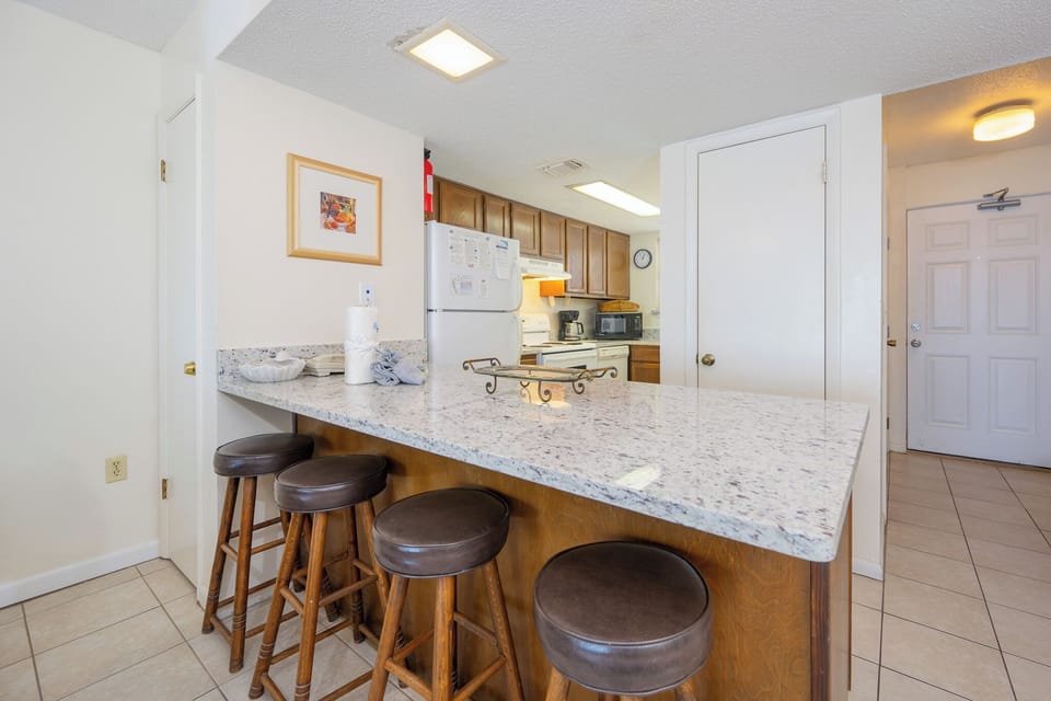 This kitchen features a spacious countertop, wooden cabinetry, and a cozy dining area with colorful chairs, perfect for meals