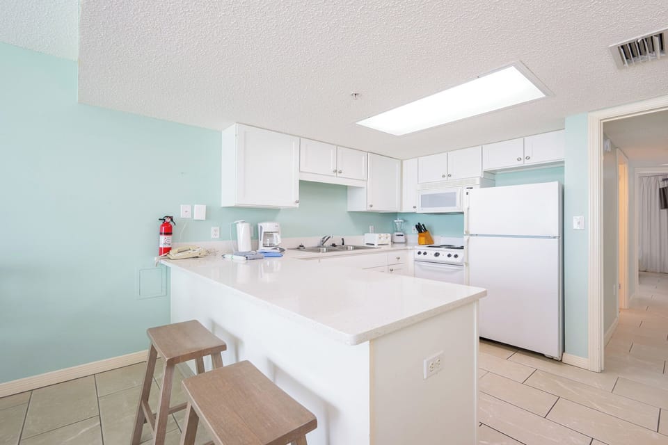 Prepare meals in this kitchen, featuring a breakfast bar with stools and essential appliances for your convenience
