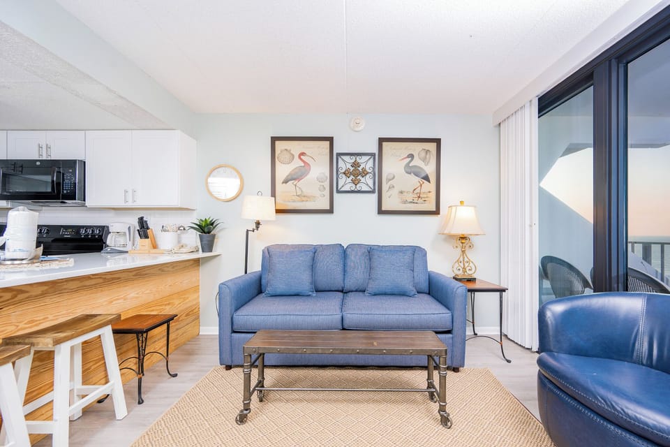 This inviting living area features a comfortable blue sofa, stylish decor, and a stunning beachfront view through large windows