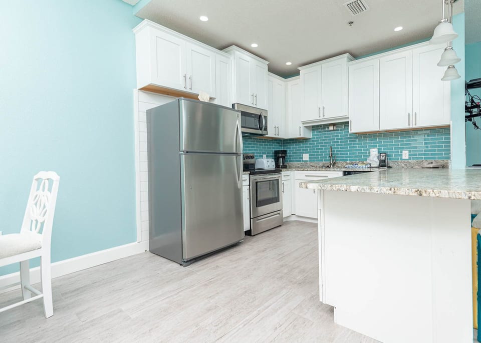 Cheerful kitchen featuring stainless appliances, granite counters, vibrant backsplash, and modified bar with stylish lighting