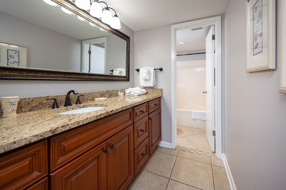 Elegant master bath featuring a spacious granite countertop, dark fixtures, and a tub/shower combo